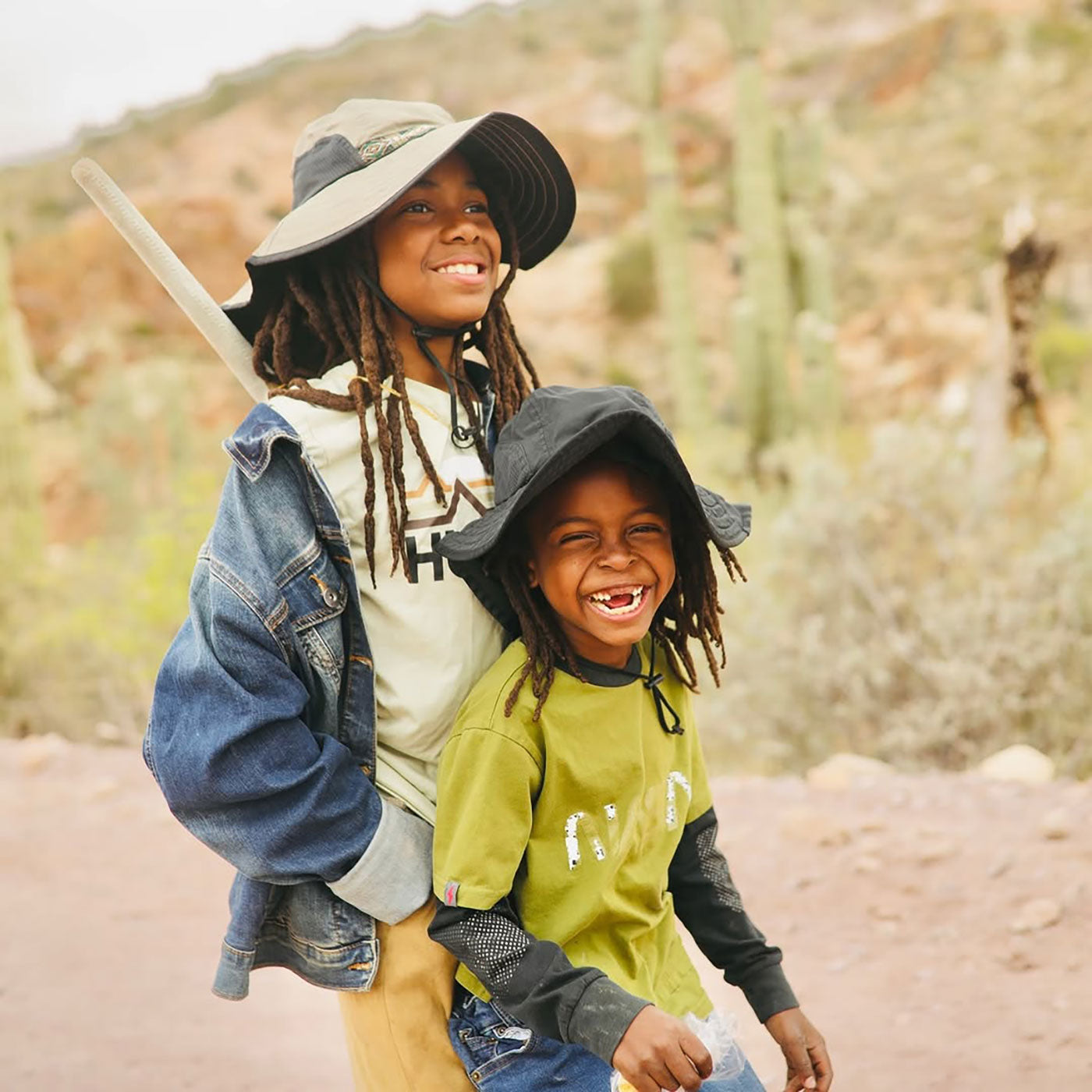 Two children outdoors in a natural setting, wearing hats and jackets.