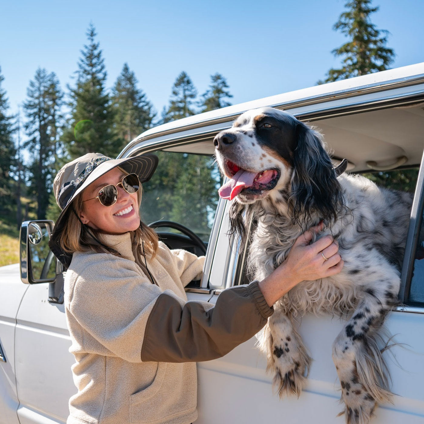 Woman with a dog in a car surrounded by trees, wearing a Sunday Afternoons Adventure Hat.