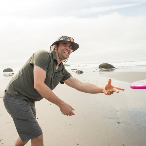A man throwing a frisbee on the beach while wearing a Sunday Afternoons Ultra Adventure Hat